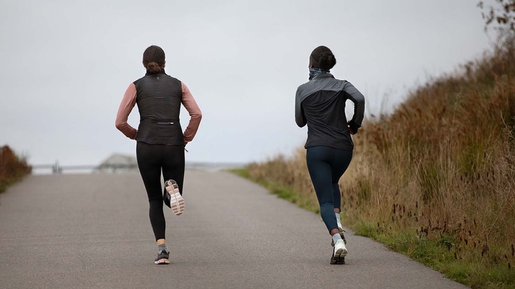 Two runners (seen from behind) running up an inclined asphalt path that passes through a natural grassland area