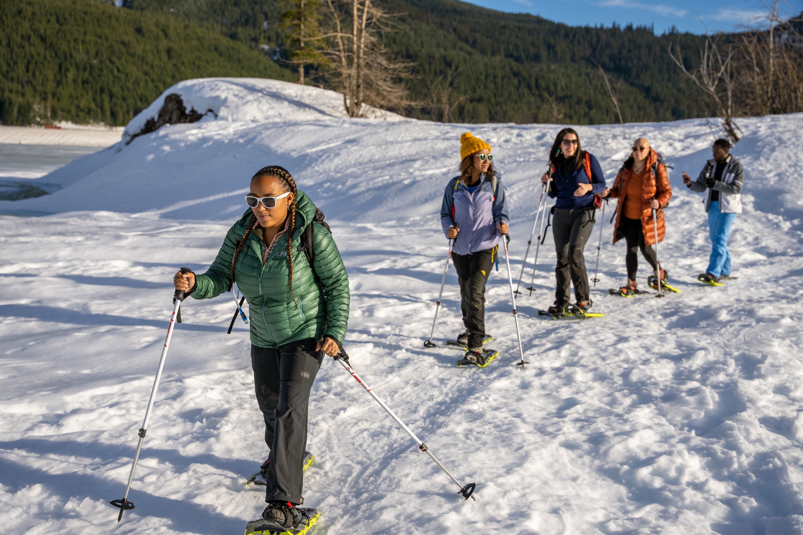 Five people dressed in layers snowshoe on a snowy trail