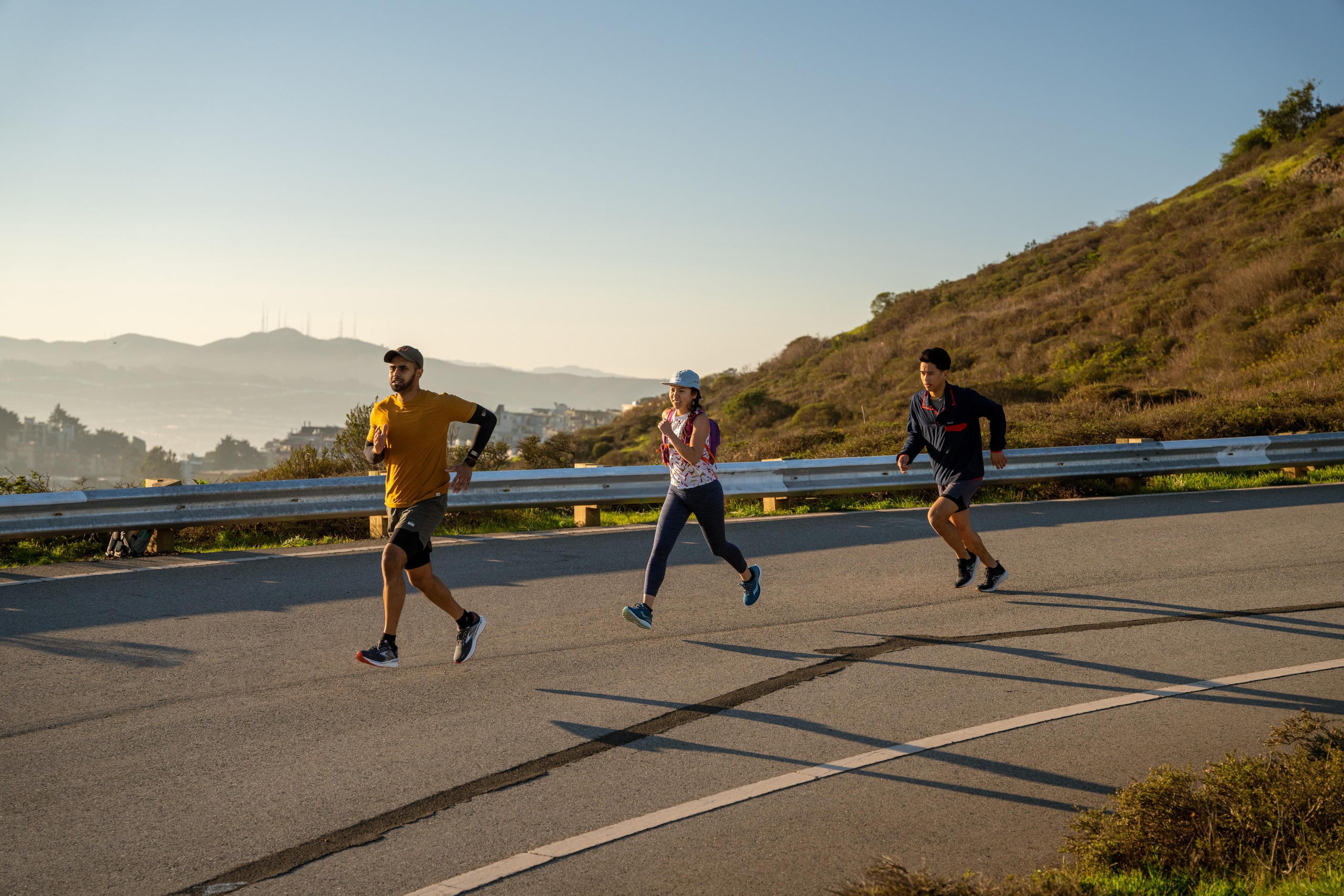 Three people running down a road with a mountain landscape in the background.
