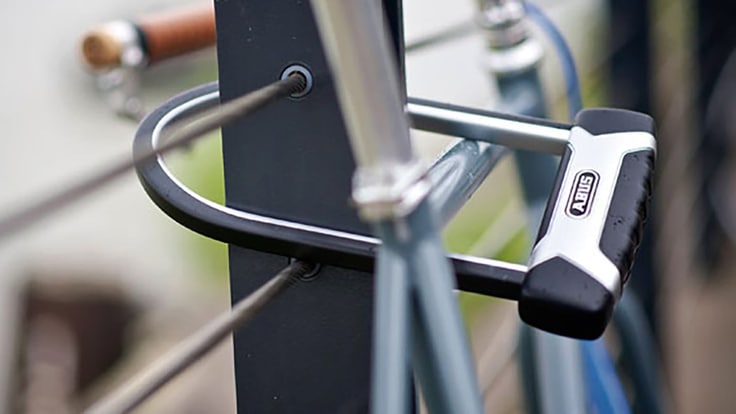 Close up of a U lock connecting a bike to a cable fence.