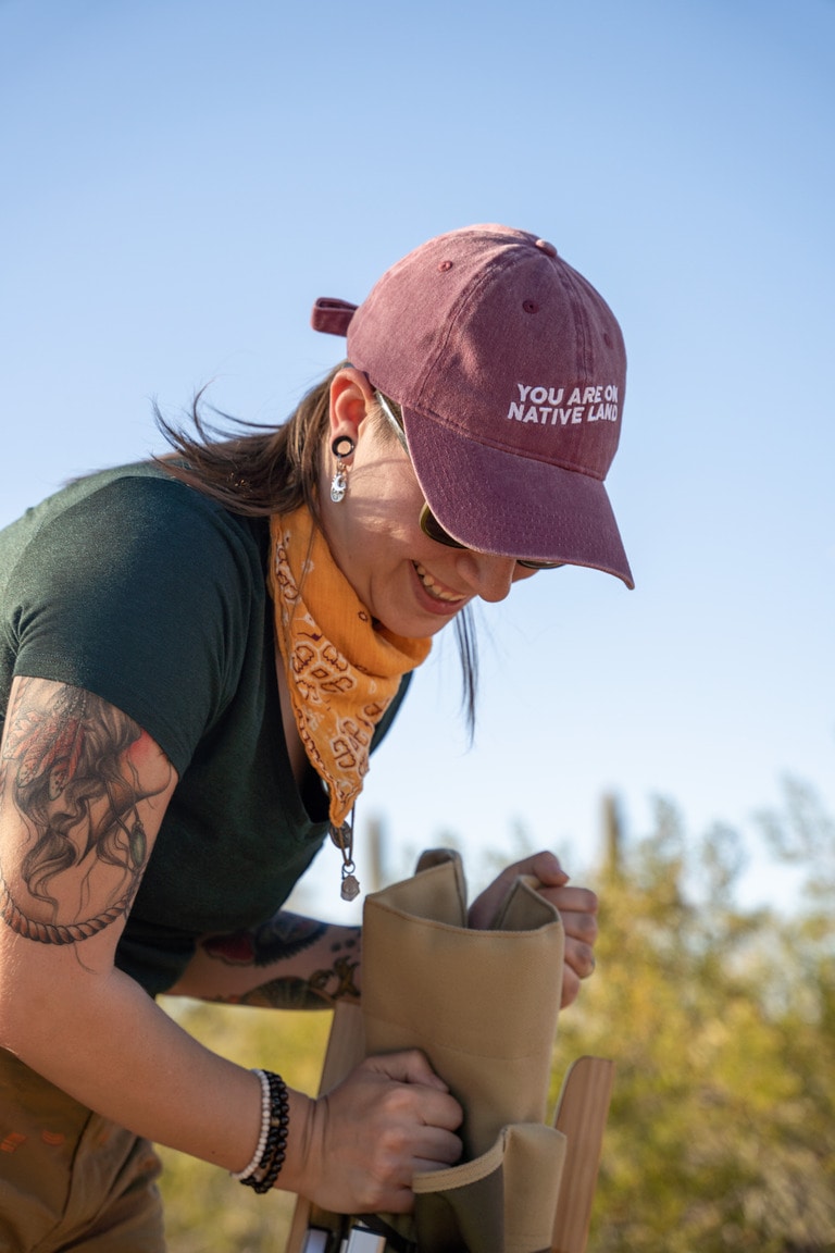 A person wearing a brimmed cap and an orange bandana unpacks a folded camp chair outside.