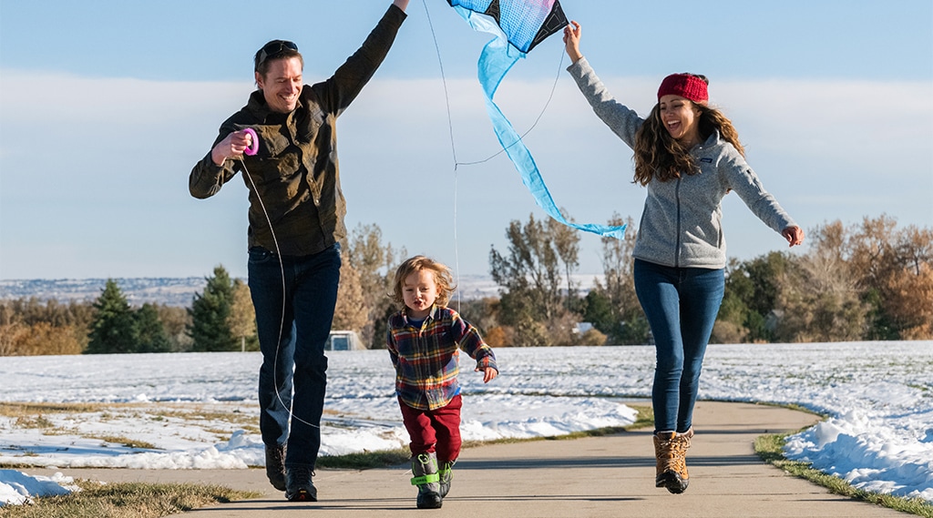 Two adults fly a kite with a young kid.