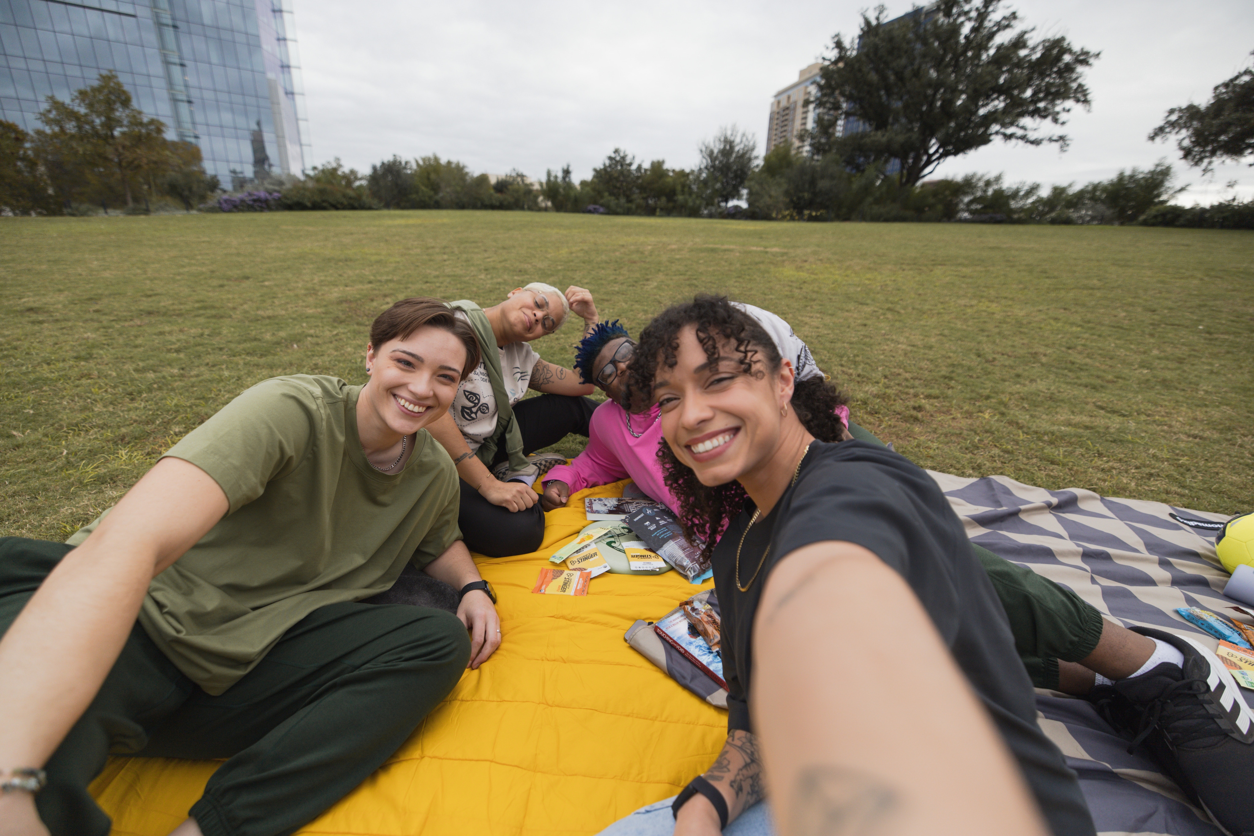 Four smiling people sit on a blanket at an urban park