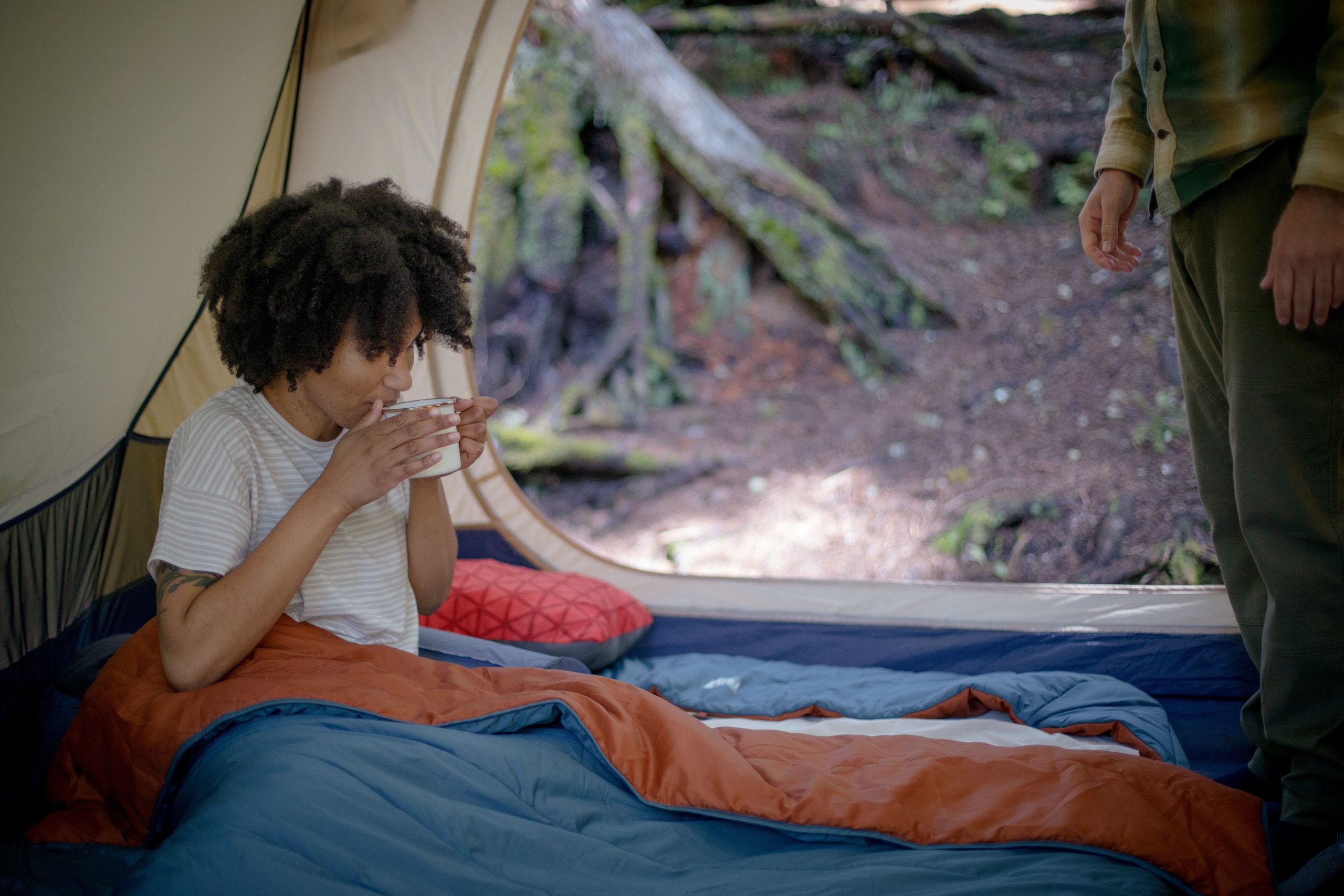 A woman drinks coffee from inside her tent.