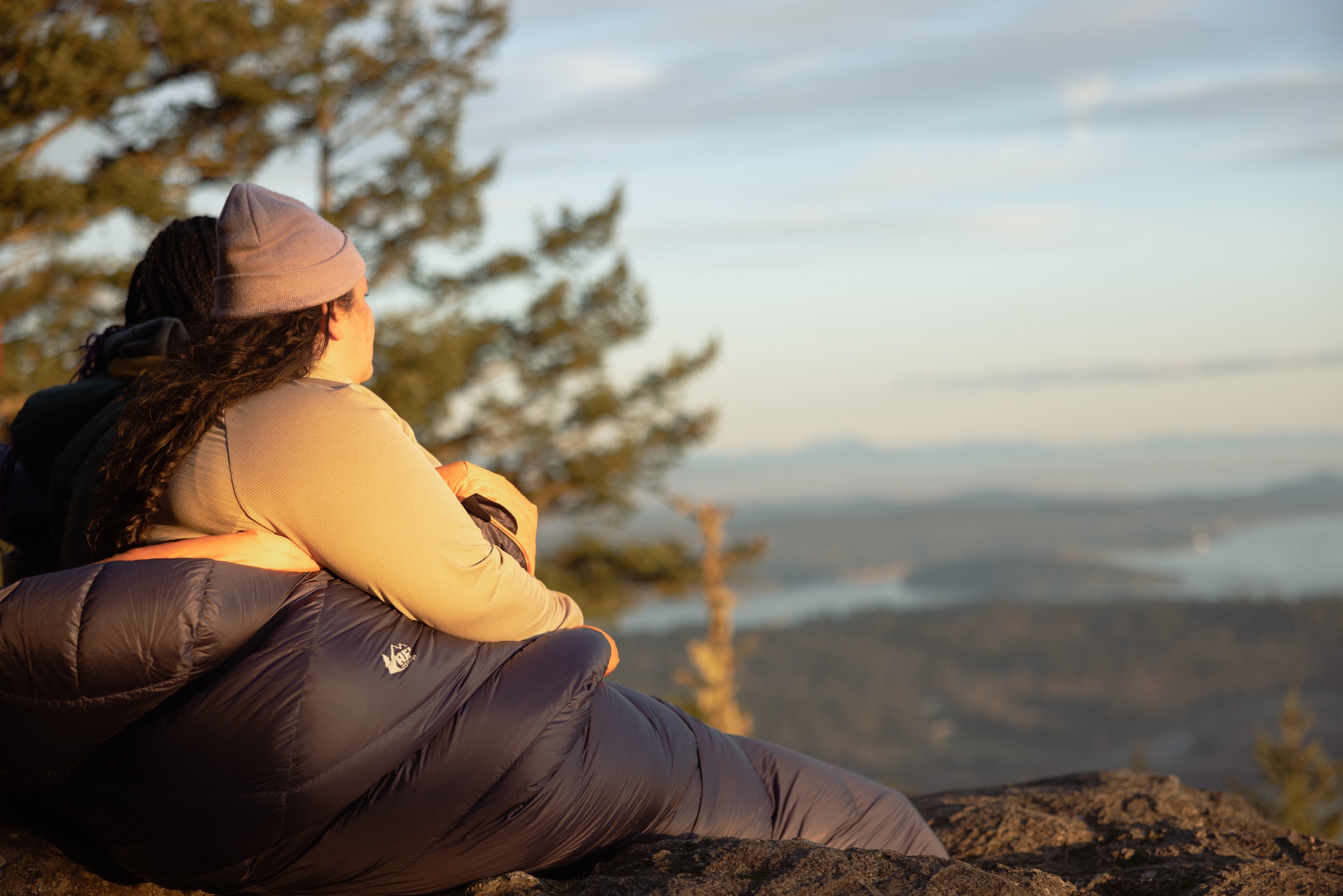 A person wrapped in a sleeping bag gazes out at the view from a mountain.
