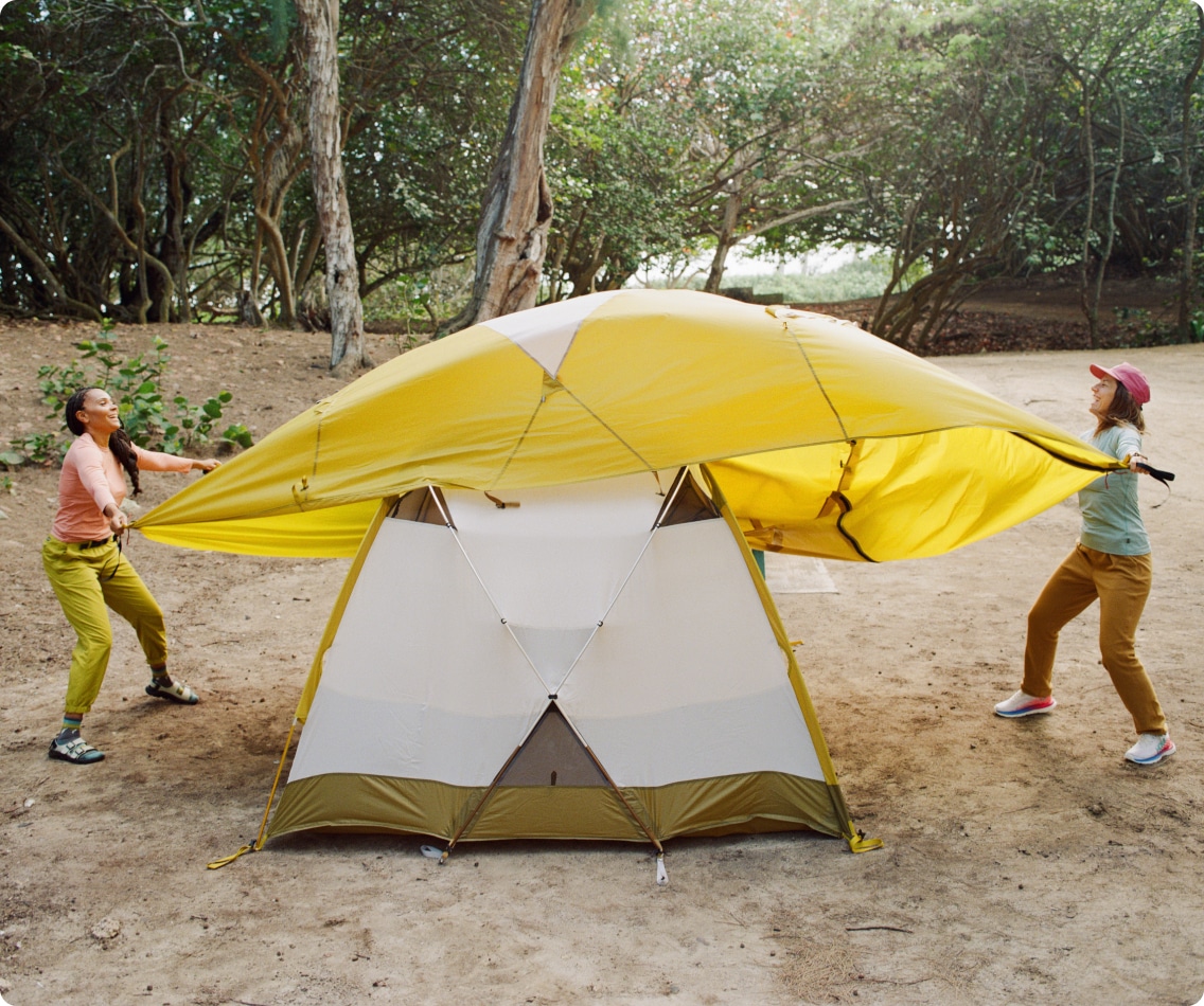 Two people put the rain fly on a tent.