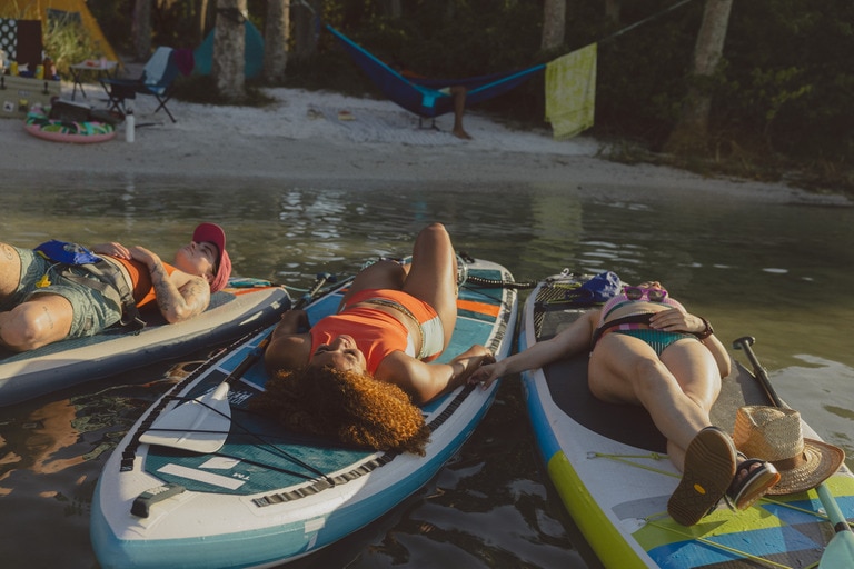 Three people lie on separate paddle boards of various lengths and widths.