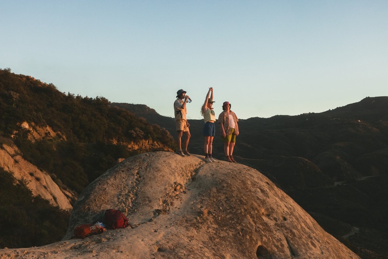three people standing on top of rock at sunset