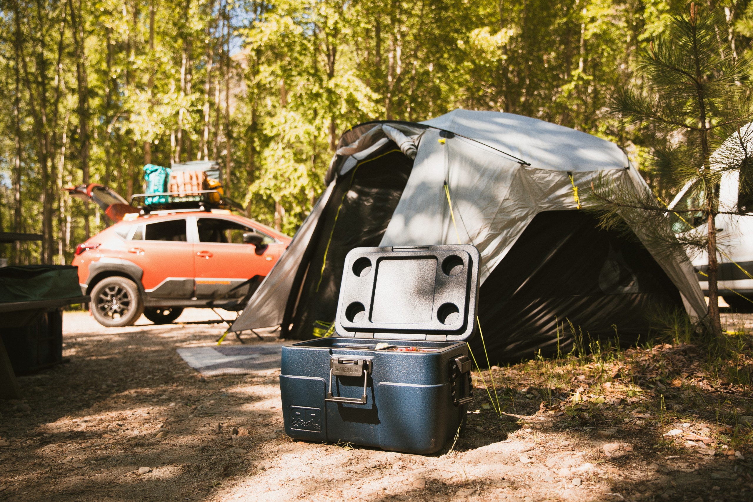 A hard-sided cooler is displayed in front of a tent at a campsite