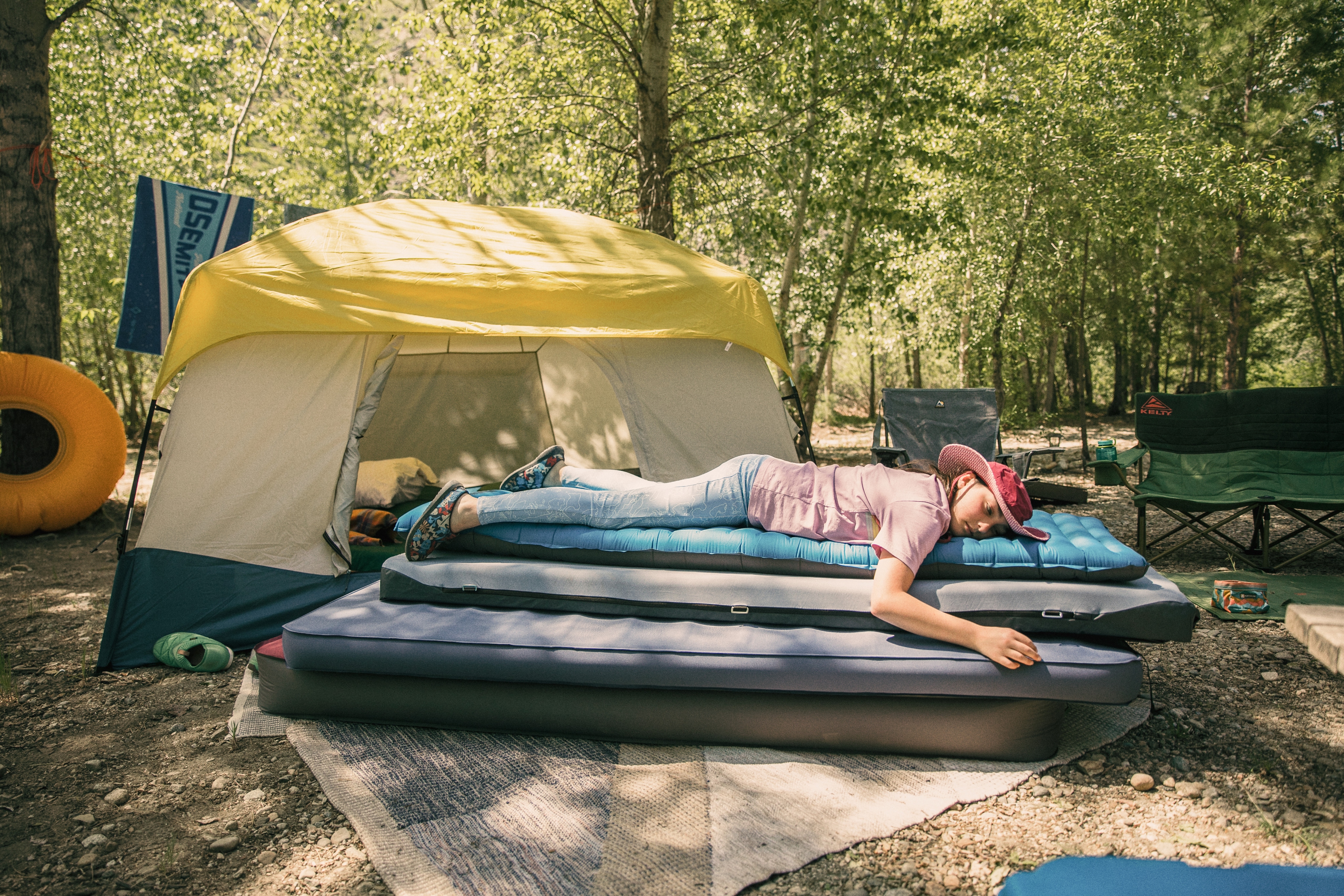 A person laying on top of a stack of sleeping pads in front of a tent.