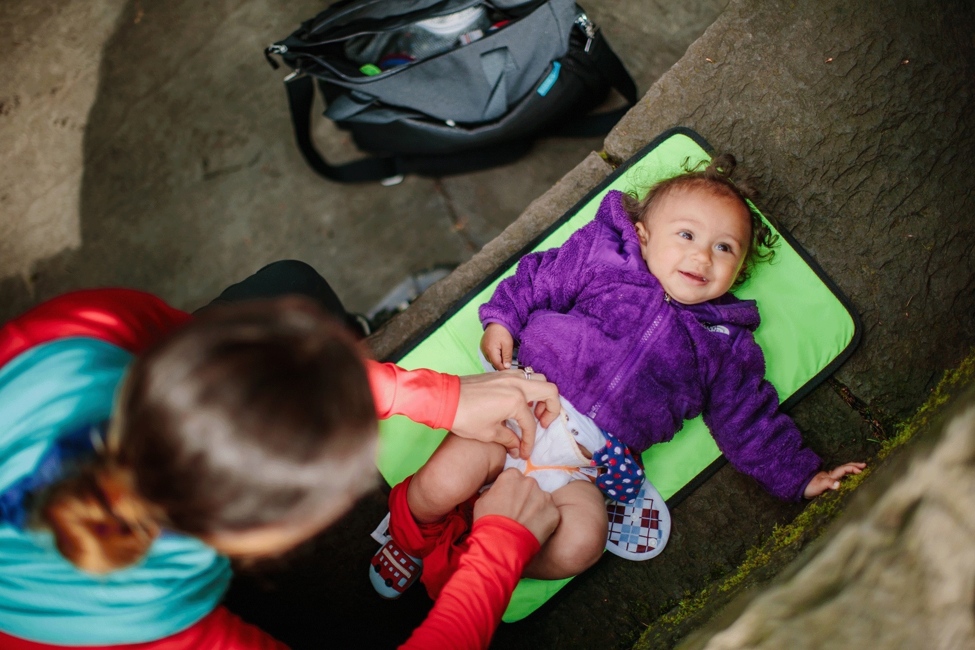 A person changes the diaper on a baby on lies on a green mat.