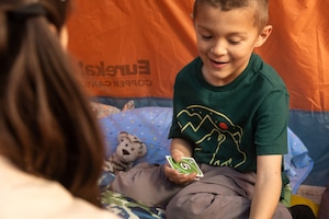 A young boy in a green shirt playing cards in a tent.