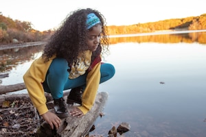 A young girl at the edge of a lake looking into the water.