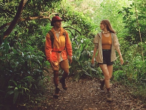 A man in an orange jacket hiking through the forest with a friend.