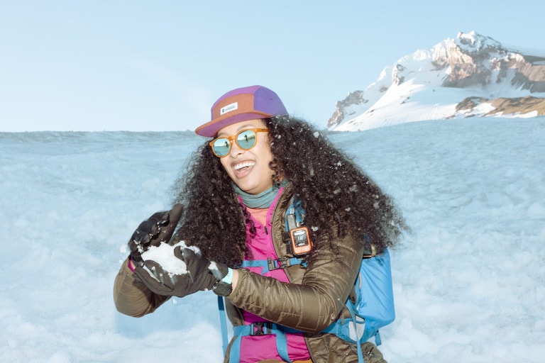 A person makes a snowball on a hill in front of a mountain