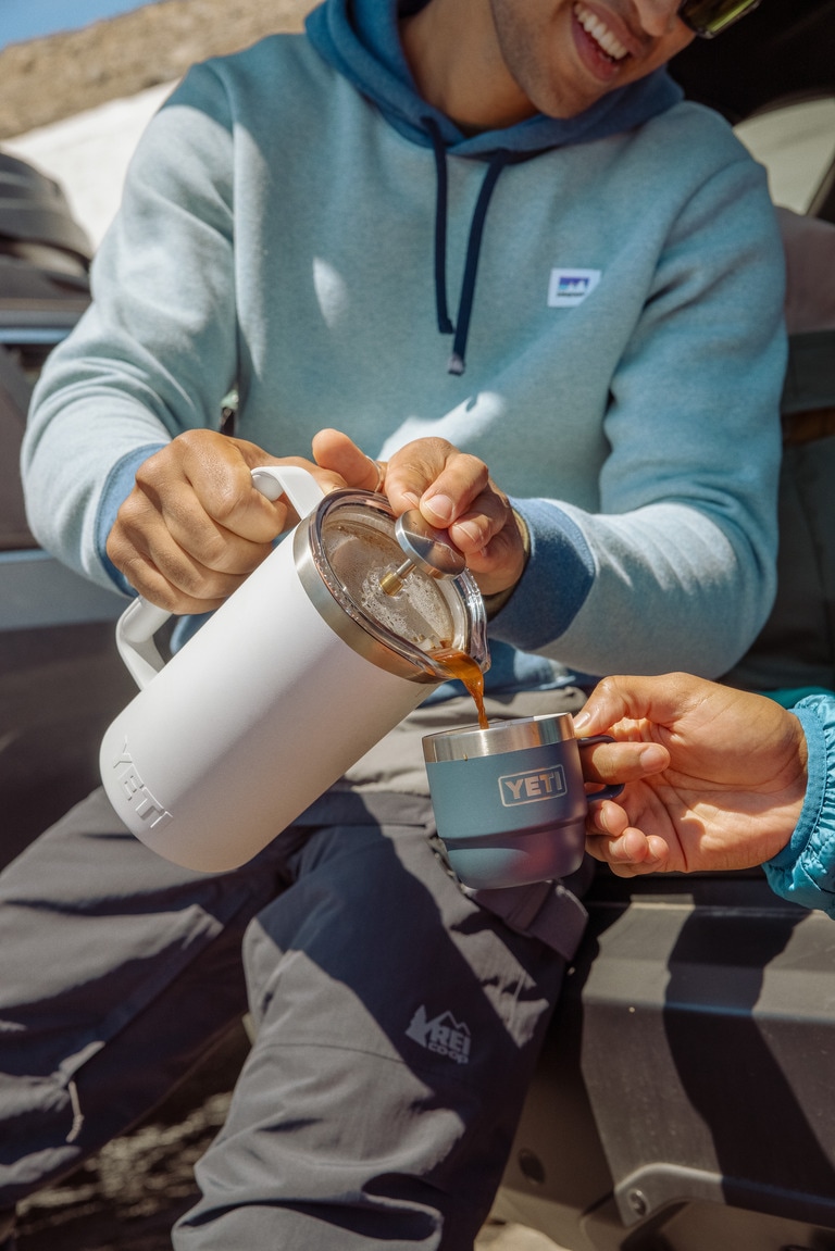 A person pours from a YETI French press into someone else's YETI camp mug