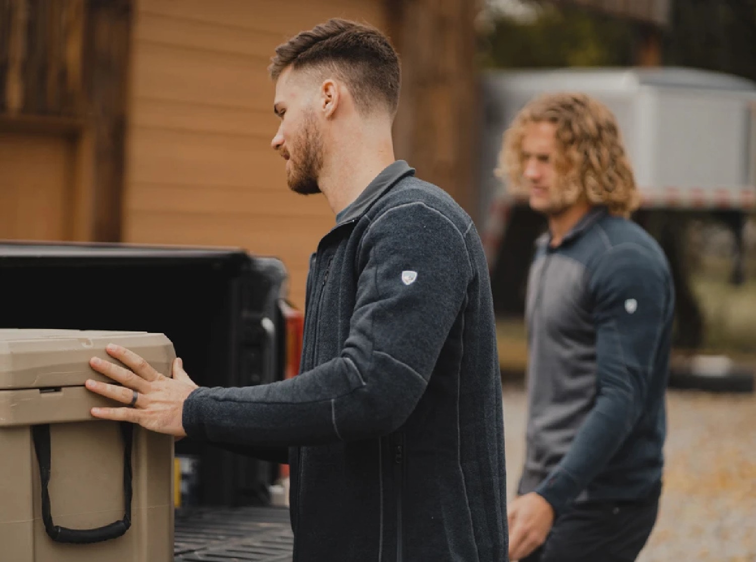 Two people wearing fleece jackets load up a flatbed truck.