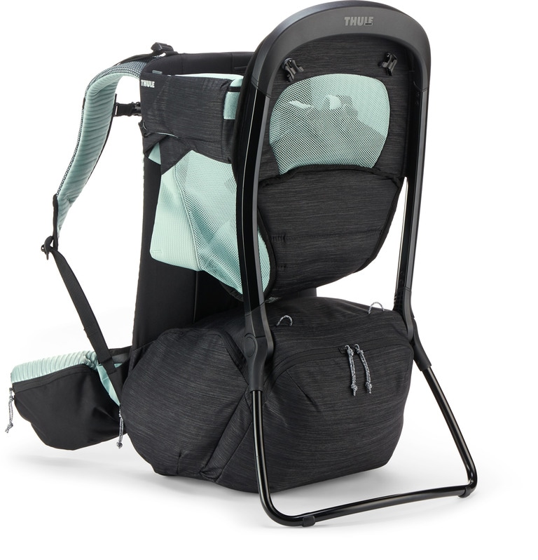 A child carrier backpack with black components and green mesh standing up on its kickstand against a white background