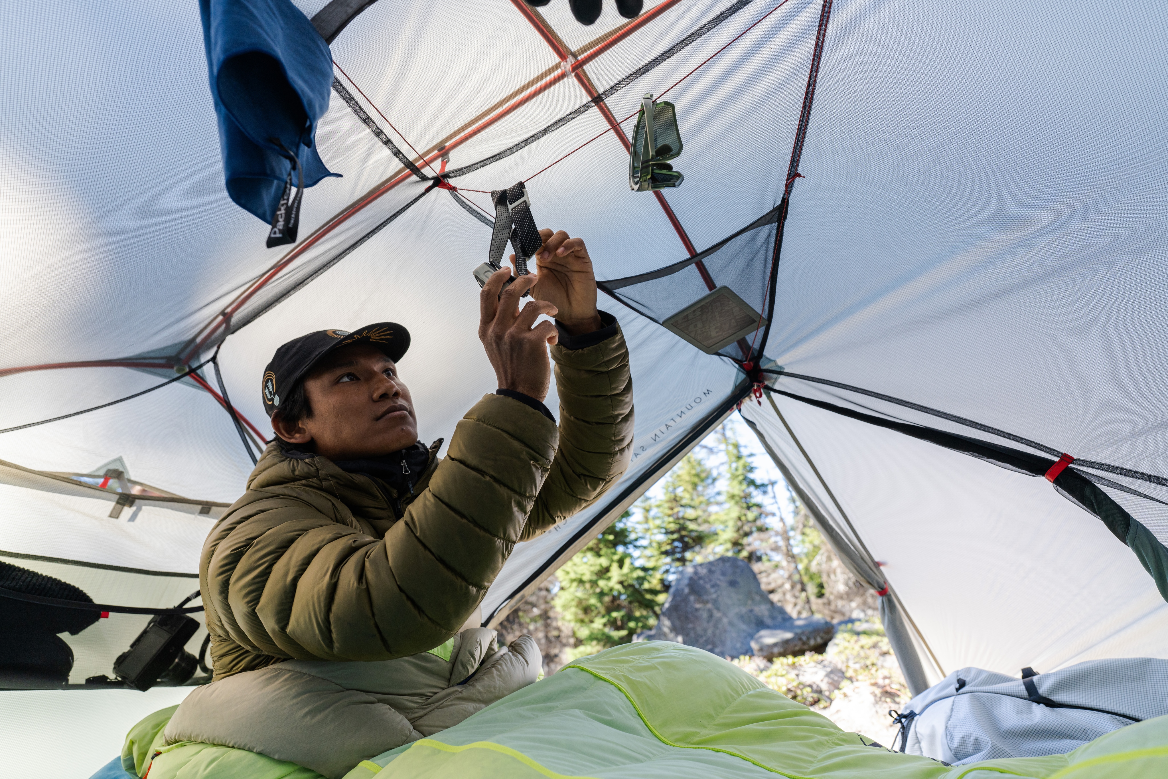 A person adjusts their camp accessories inside their tent.
