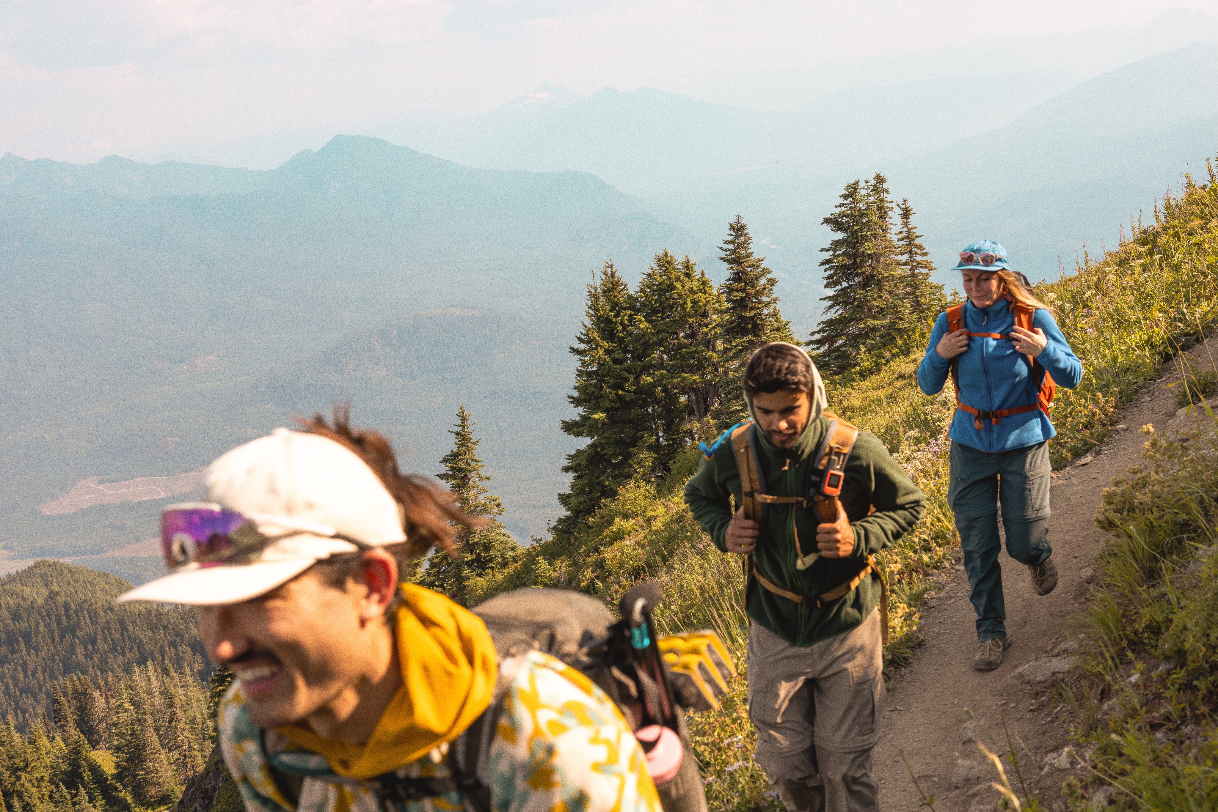 Three people hike down a hill in fleece clothing.