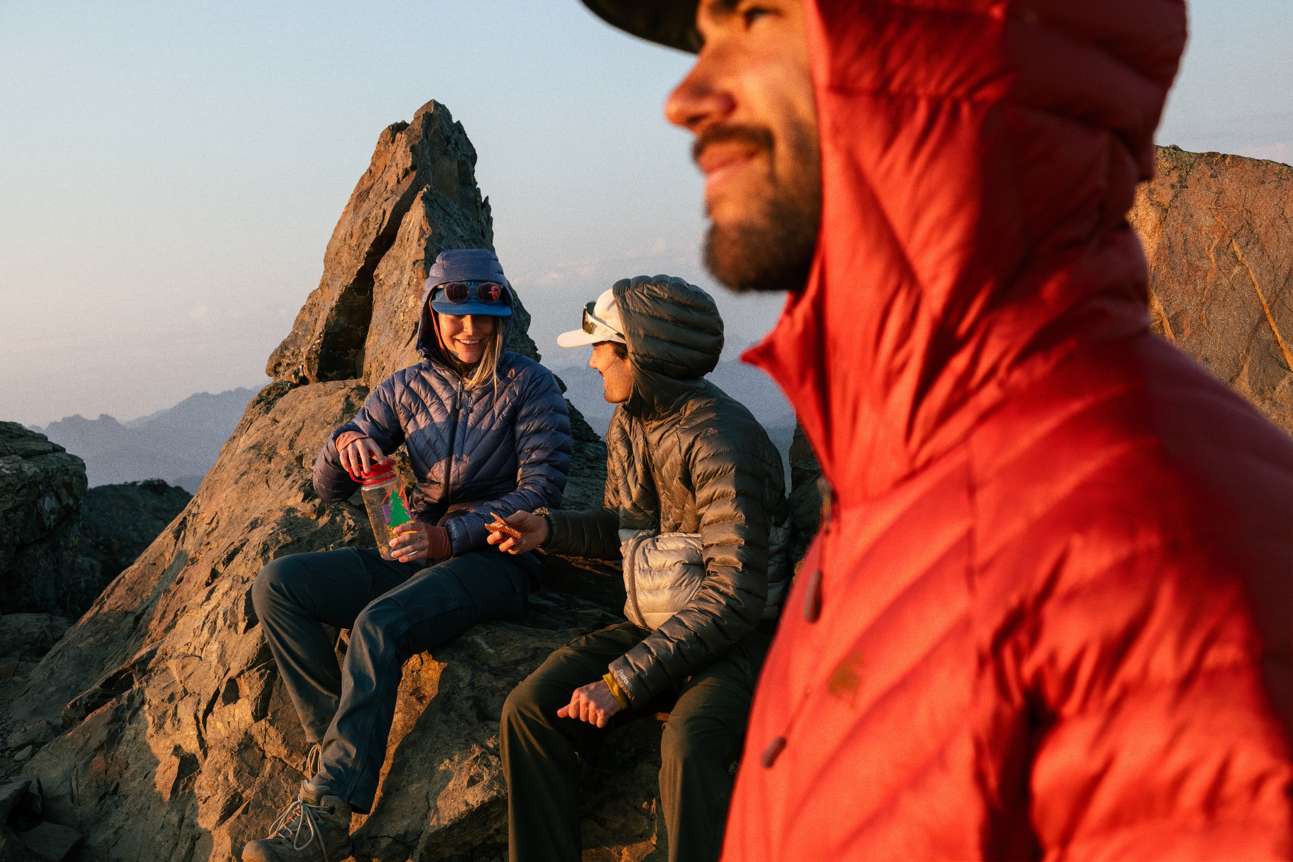 Three hikers on the summit stay warm in the REI Co-op Magma 850 Hoodie