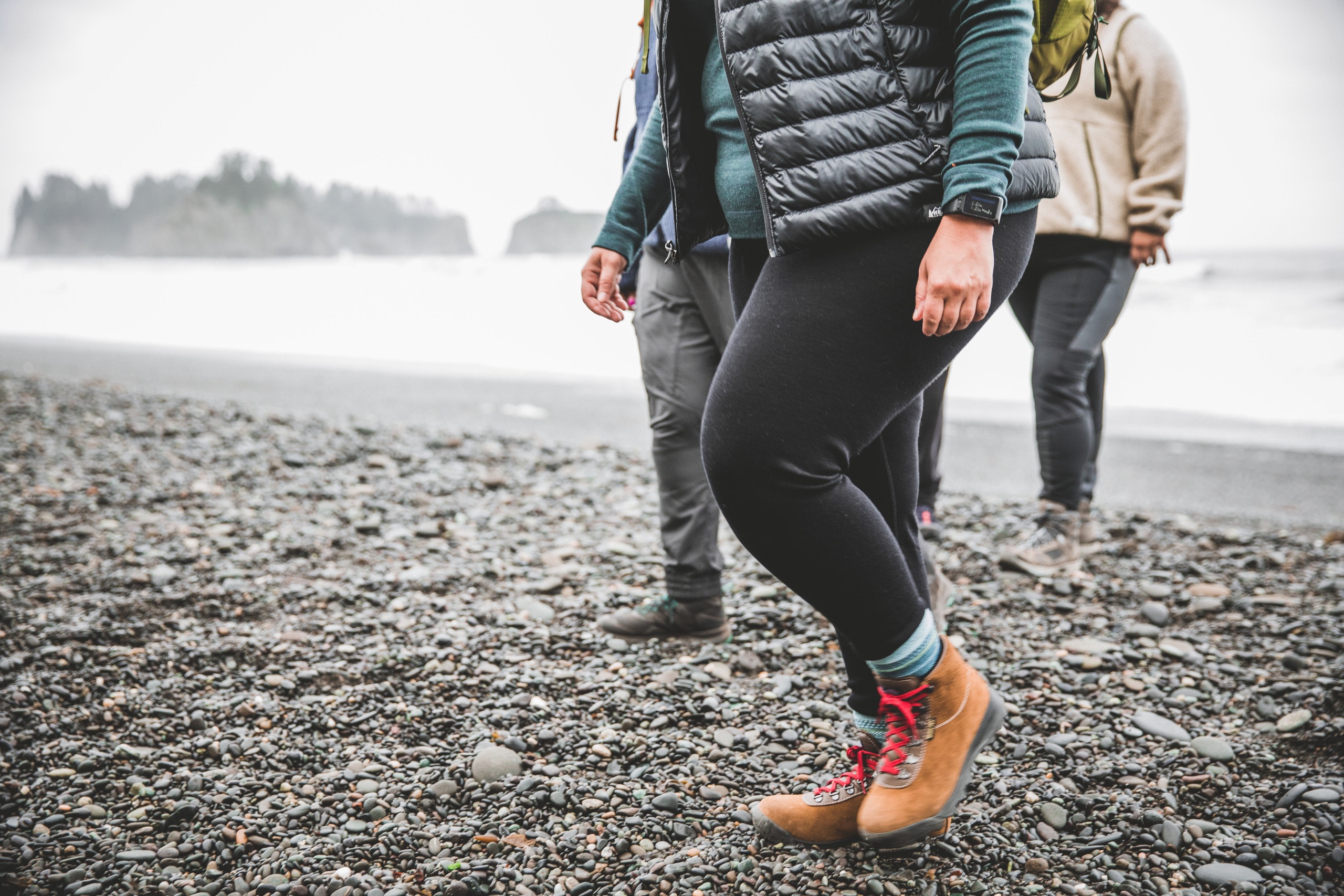 Three people walk on a rocky beach wearing hiking apparel.