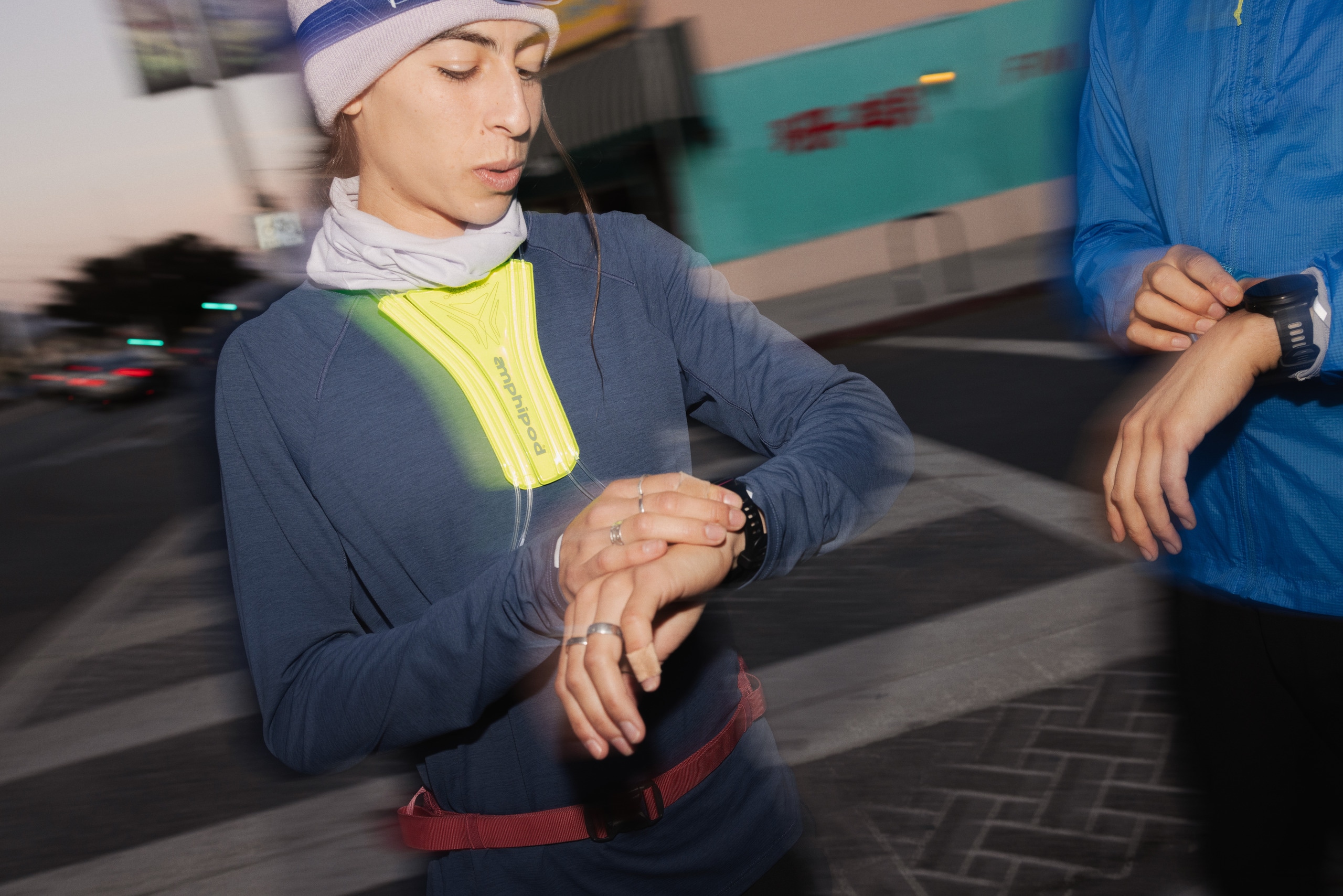 Two runners checking their watches. One wears a reflective vest from Amphipod.
