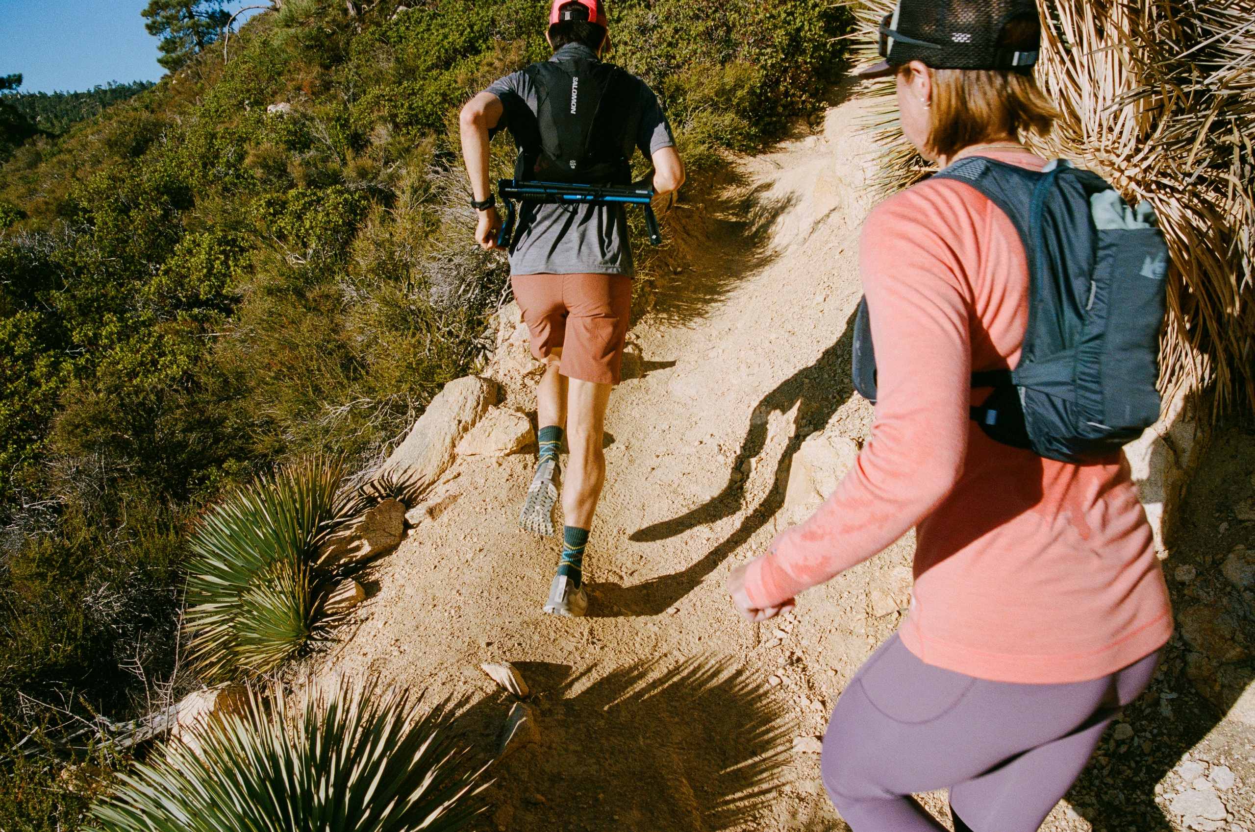 Two runners in the Salomon Adv Skin 12 and Swiftland 5 Hydration Vests, running up a mountain