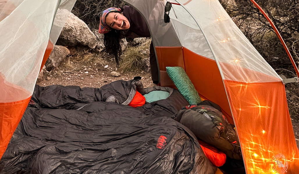 REI Co-op Member Angela R. laughing and pitching a tent at a campground.