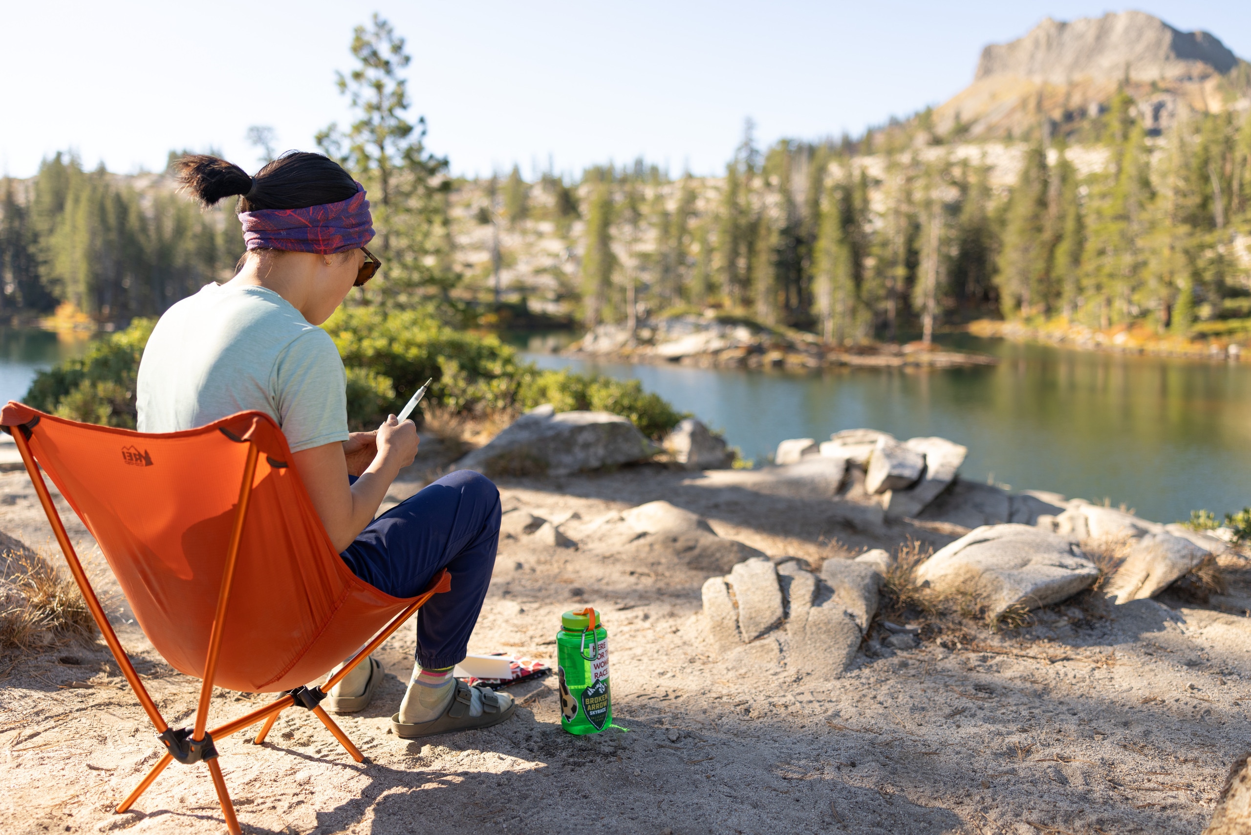 A person sits in a camp chair next to a lake
