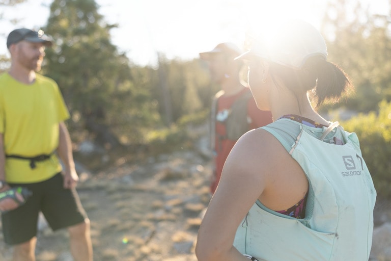 Three people stand around in running clothes with the sun beaming down on them.