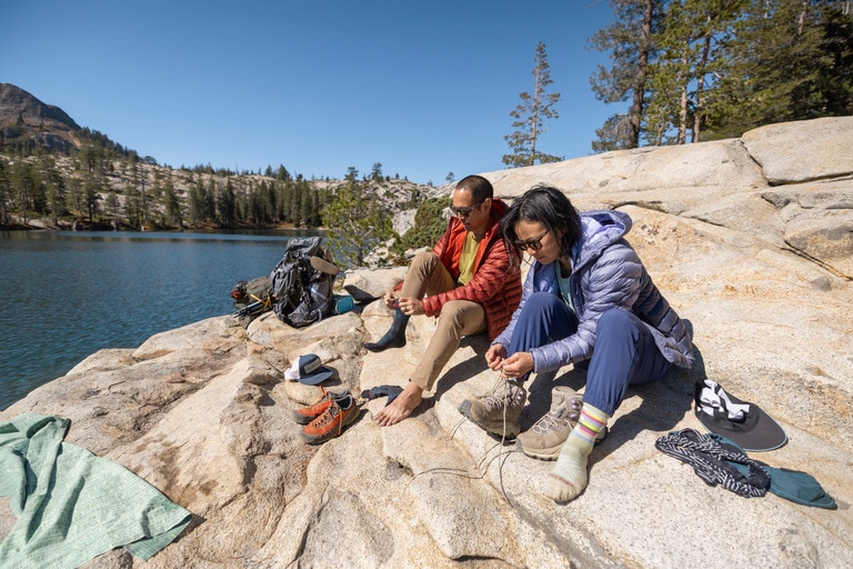 Two backpackers put shoes back on after a lake dip.