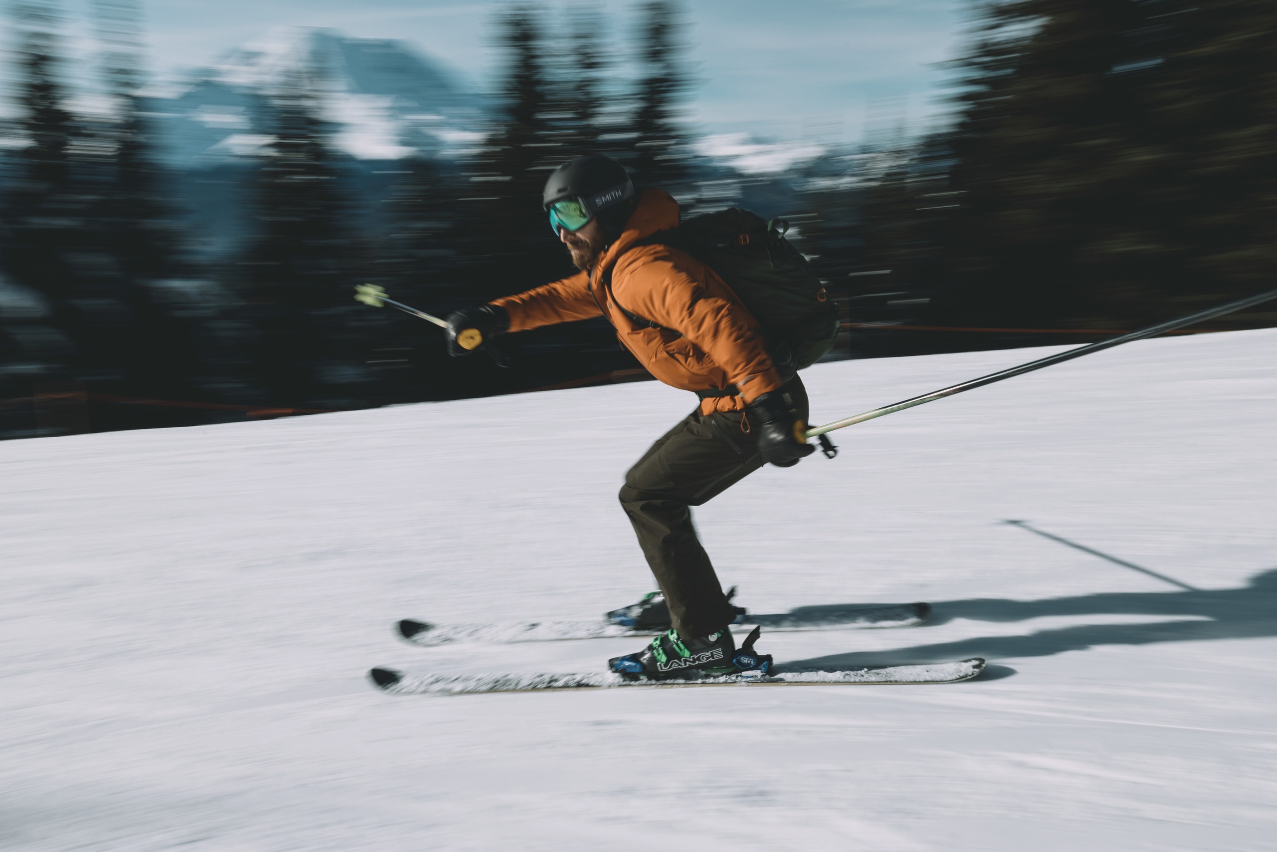 A skier wearing a black backpack cruises down slope at a ski resort.