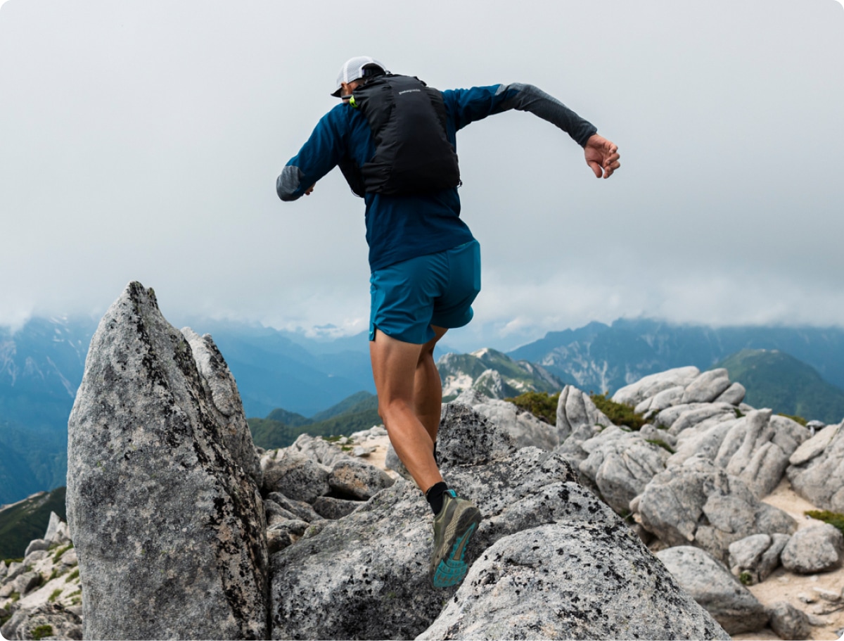 A runner dashes through a trail with snowy mountains in the background.