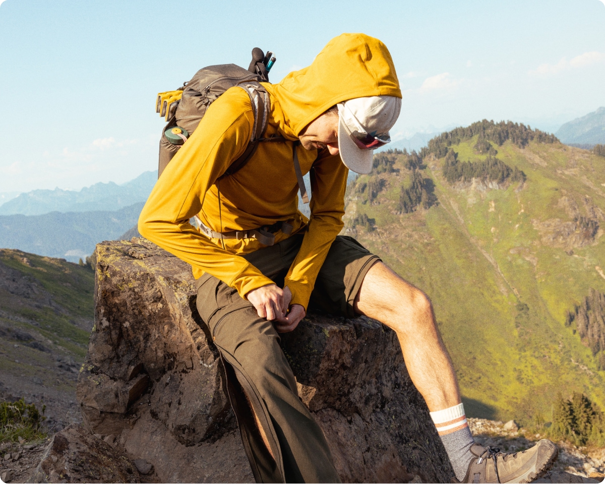 A hiker stops to unzip the legs off of their hiking pants to convert them into shorts.