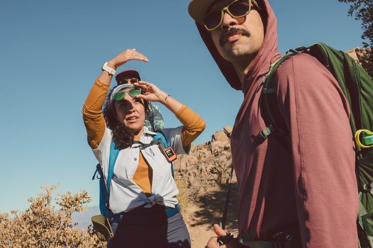 Two people hiking in hot weather wear loose clothing and sunglasses