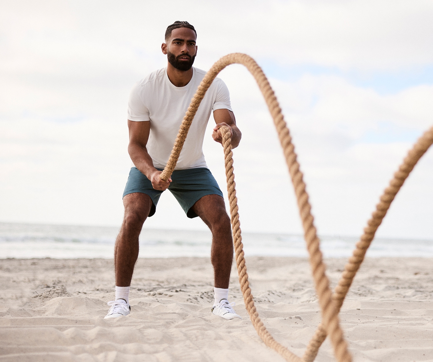 A person does a battle rope exercise on the beach