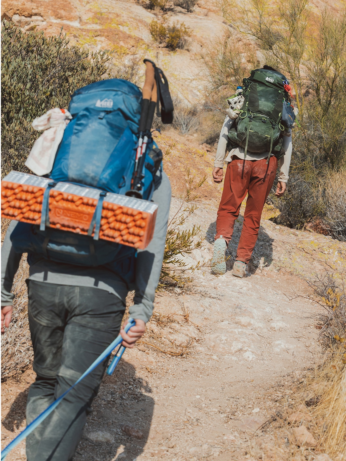 Two people hike up a rocky trail with their hiking packs.