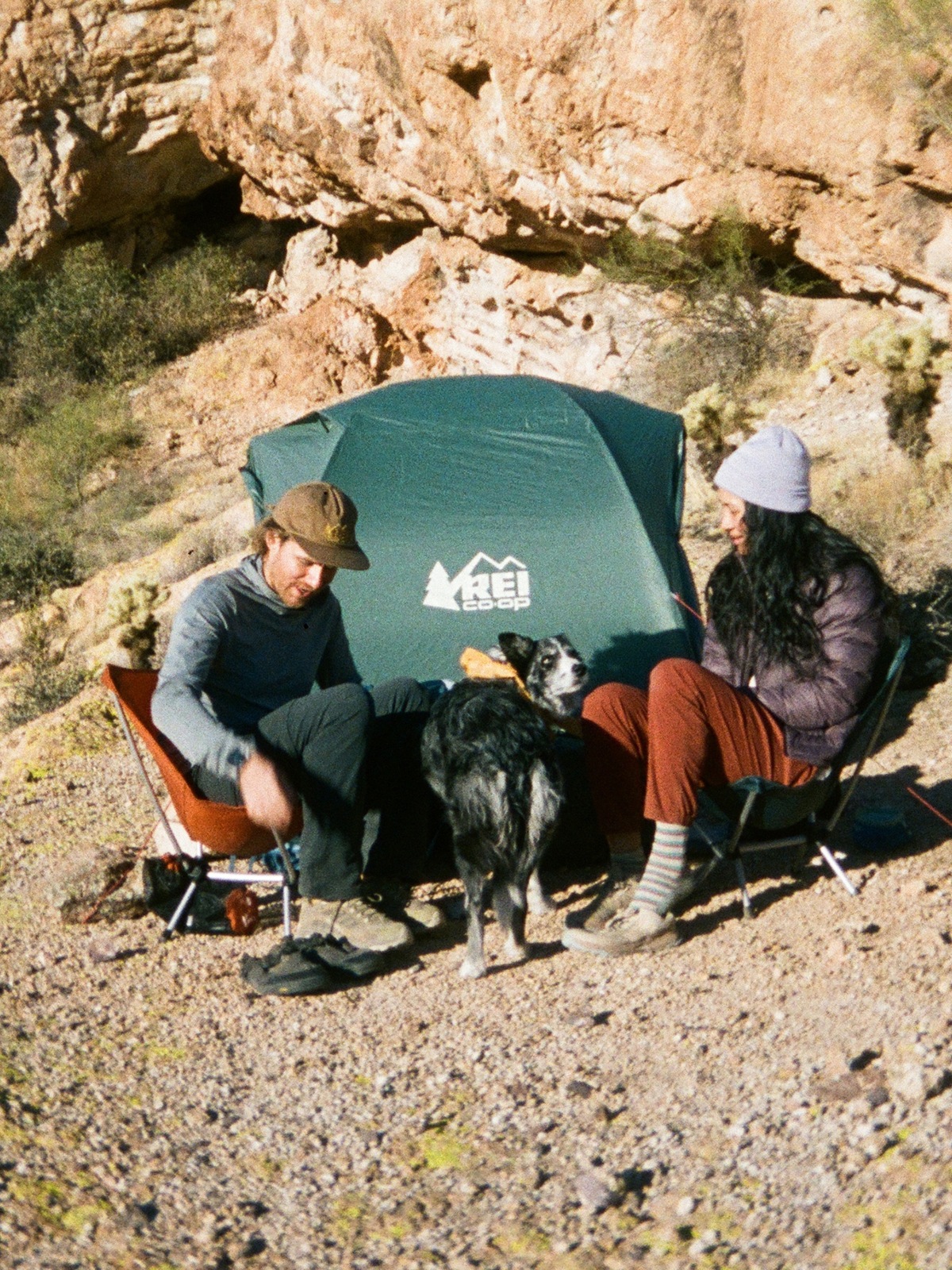 Two people and a dog sit in front of their tent.
