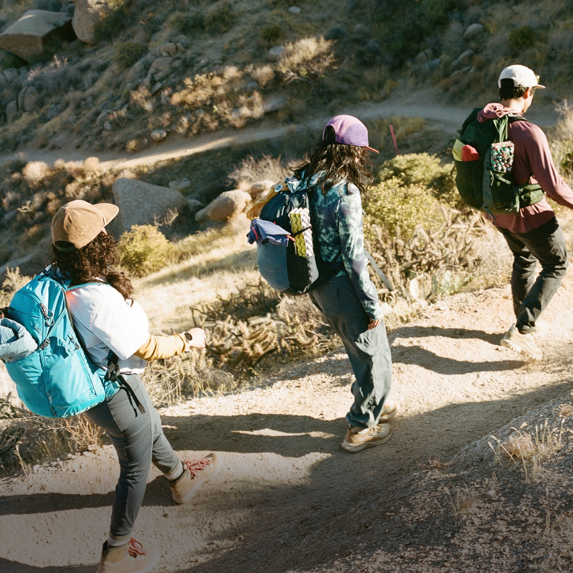Three people hike down a desert trail on a sunny day.