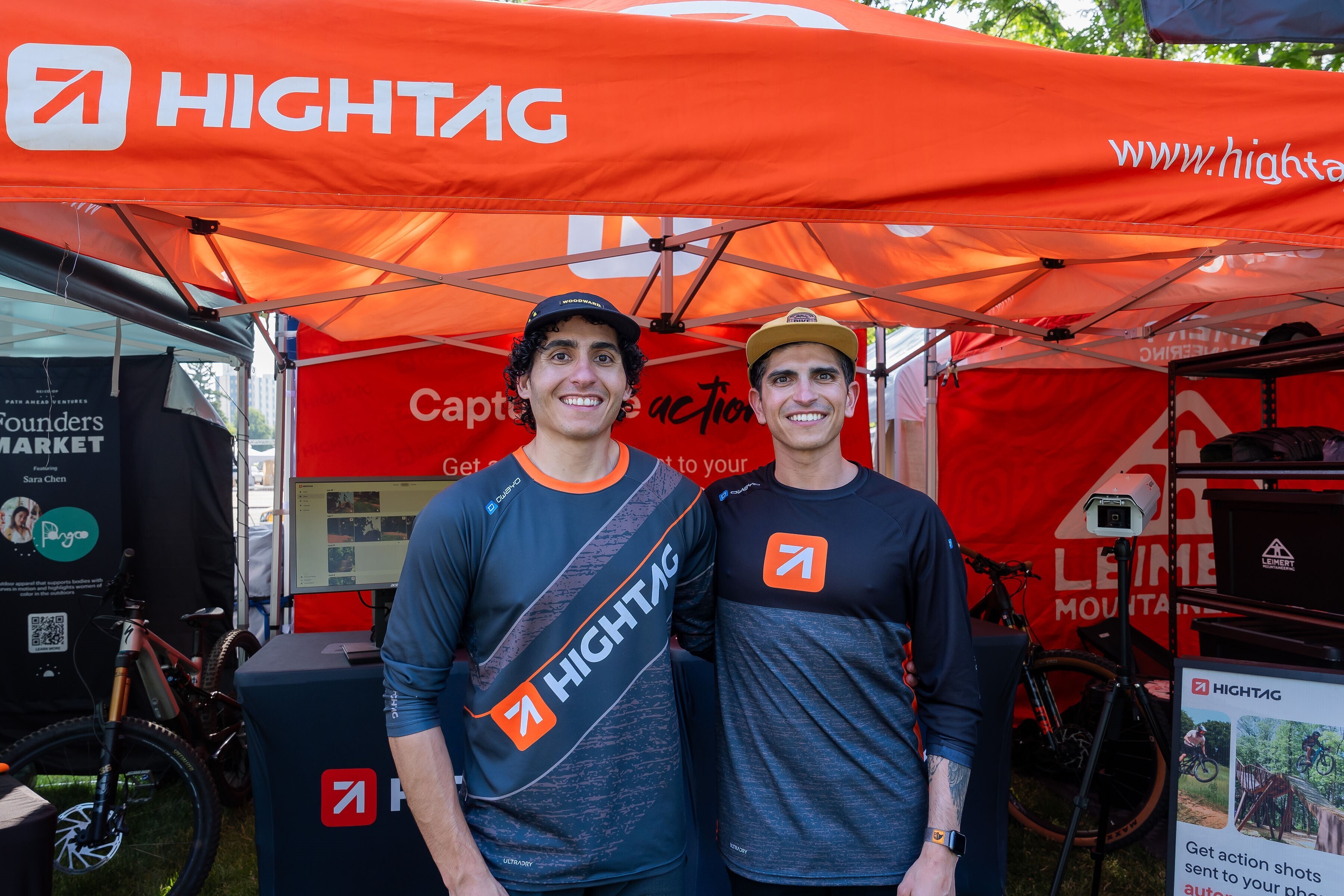 The two founders of Hightag stand, smiling in front of a tent