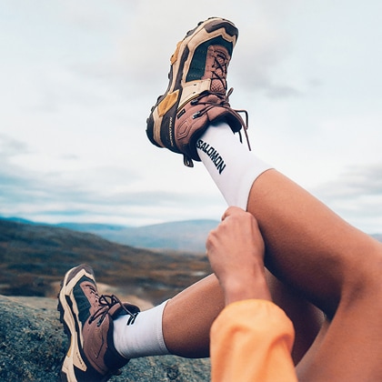 A person pulls up their socks while showing off their Salomon X Ultra 5 shoes.