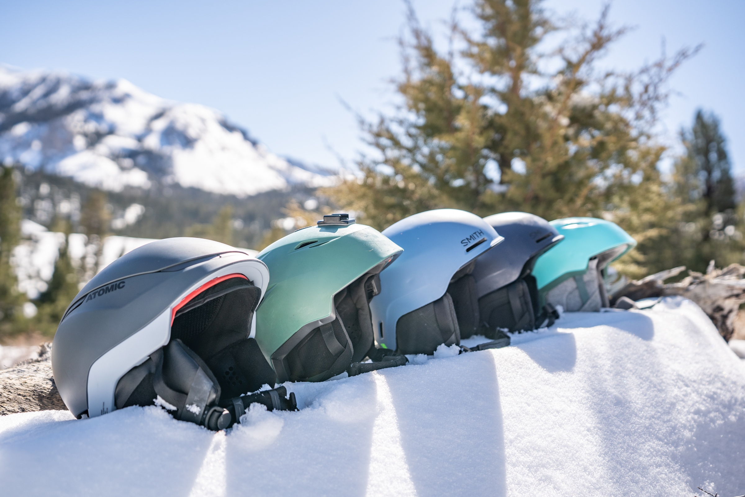 A row of ski and snowboard helmets sit on a ledge of snow
