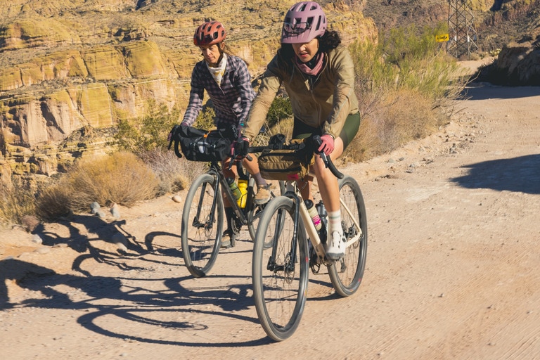 Two cyclists on their gravel bikes, riding down a dirt path.