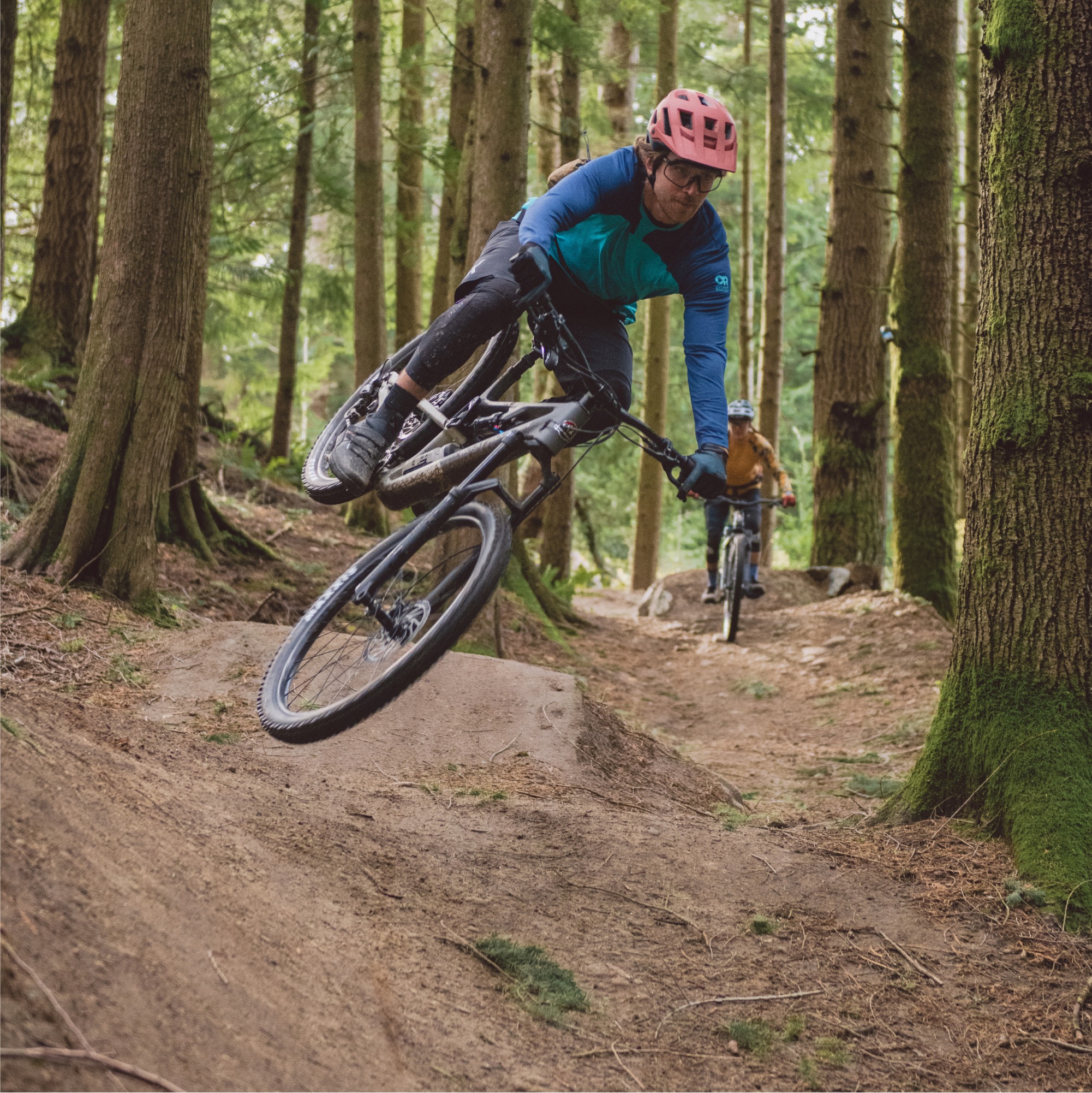Two people ride their mountain bikes through a rocky trail in a forest.