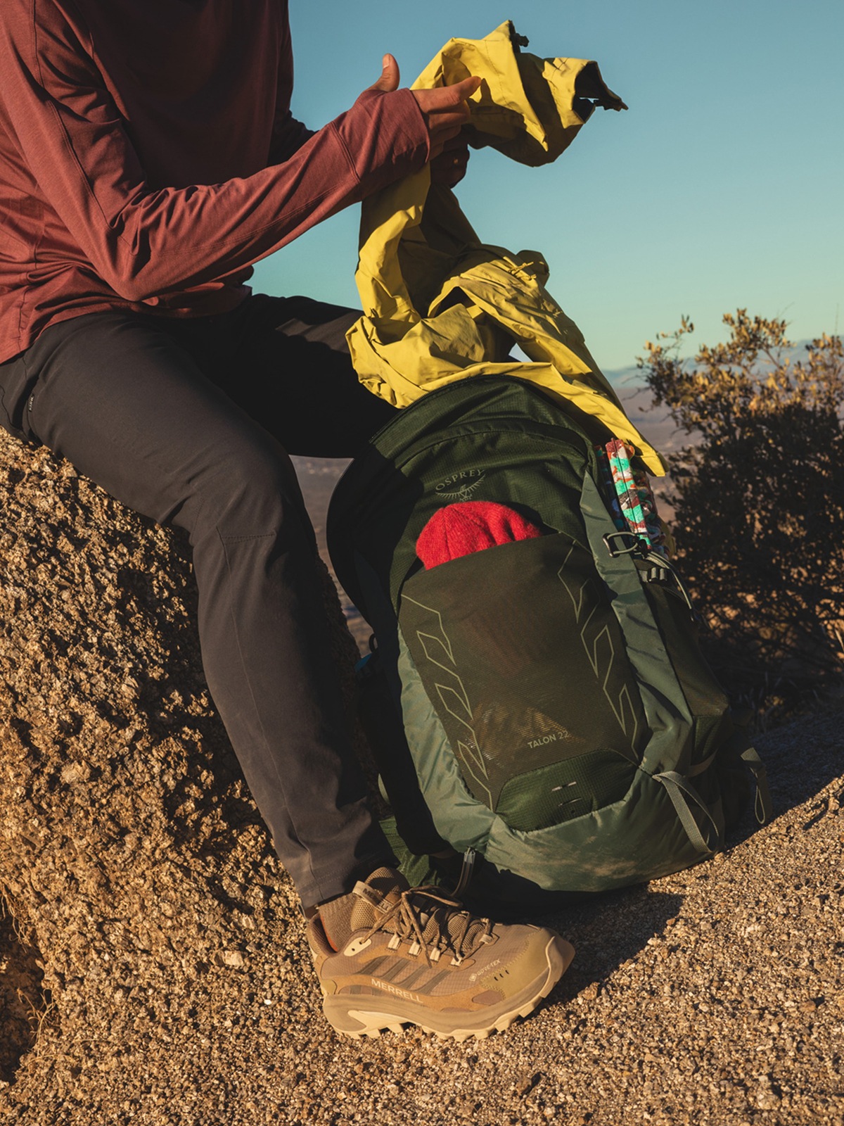 A hiker stops to grab their jacket from their Osprey pack.