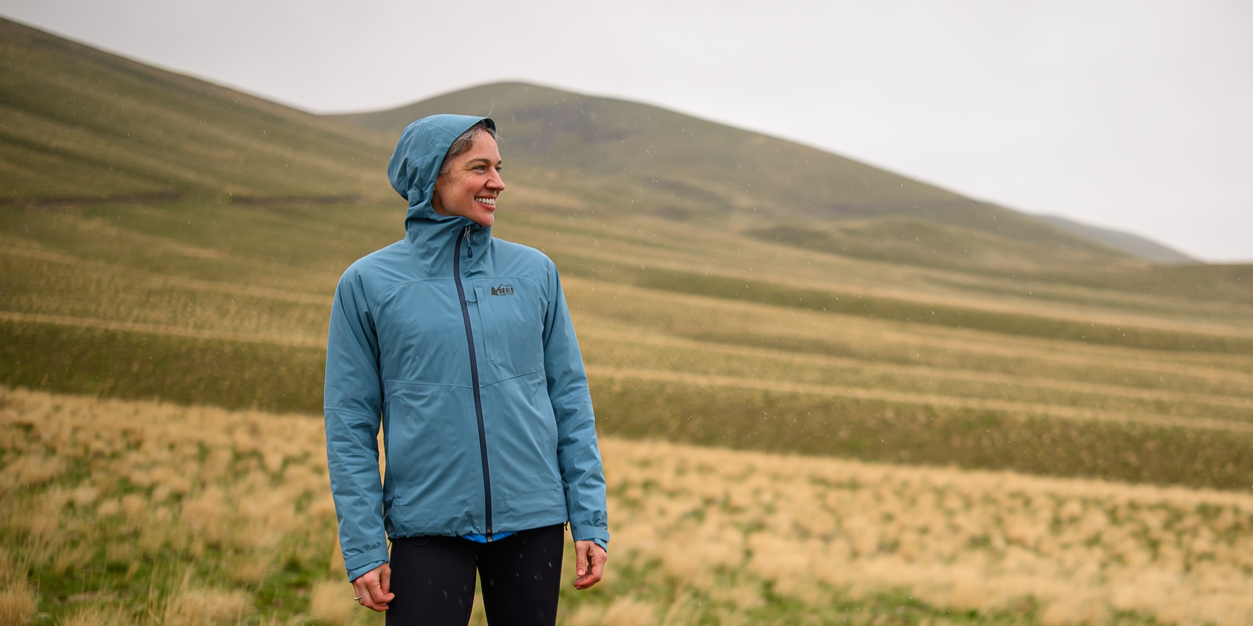 A person wearing a blue hooded rain jacket stands in a field of flowers