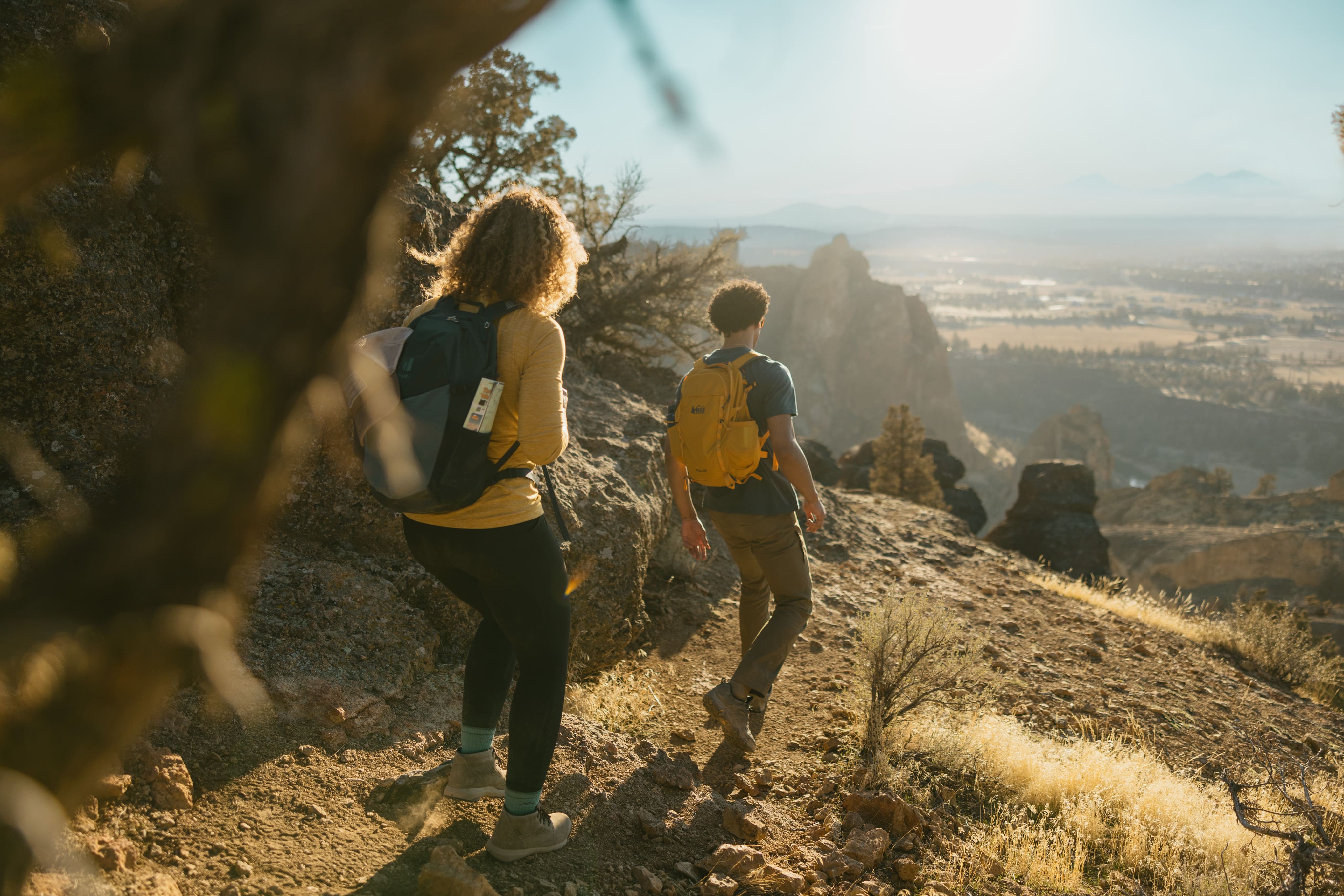 Two people hike through a dirt trail on a sunny day.