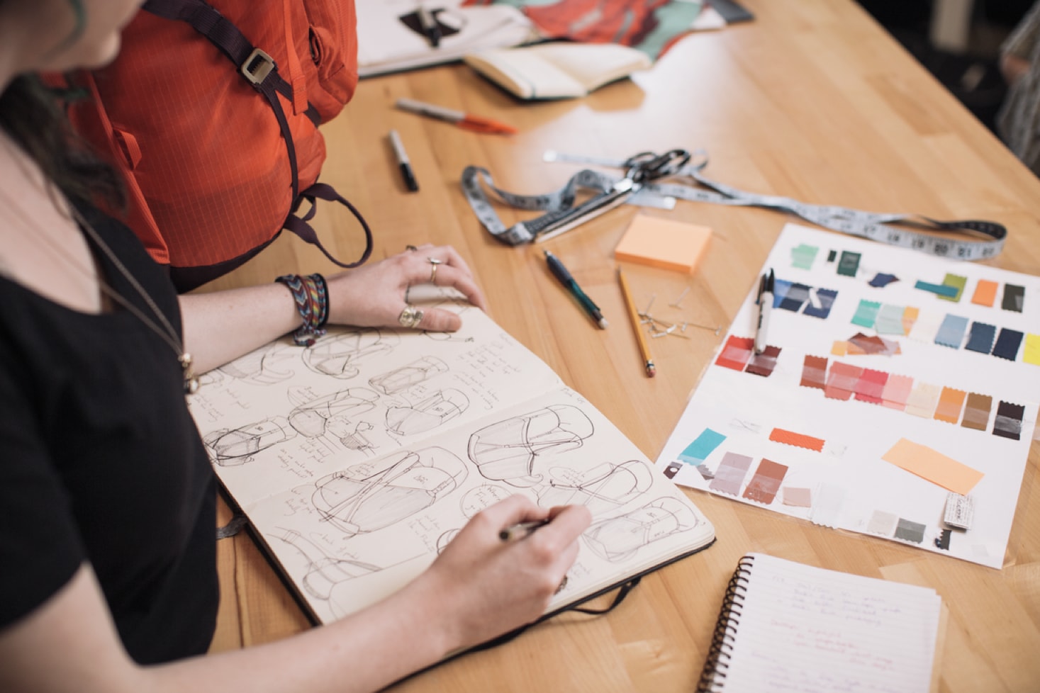 Person sketching backpack designs in sketchbook