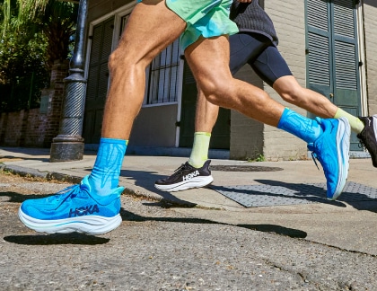 Two people run through the street in their HOKA Clifton shoes.